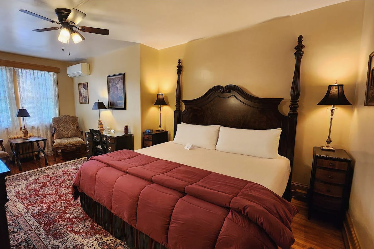 Habitación de hotel con una cama grande, un escritorio, una silla, un ventilador de techo y dos lámparas de noche.