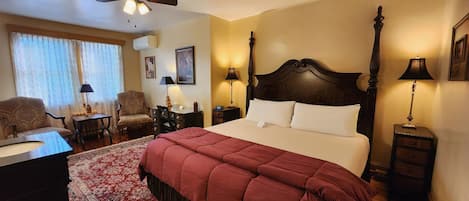A hotel room with a large bed, a desk, a chair, a ceiling fan, and two bedside lamps.