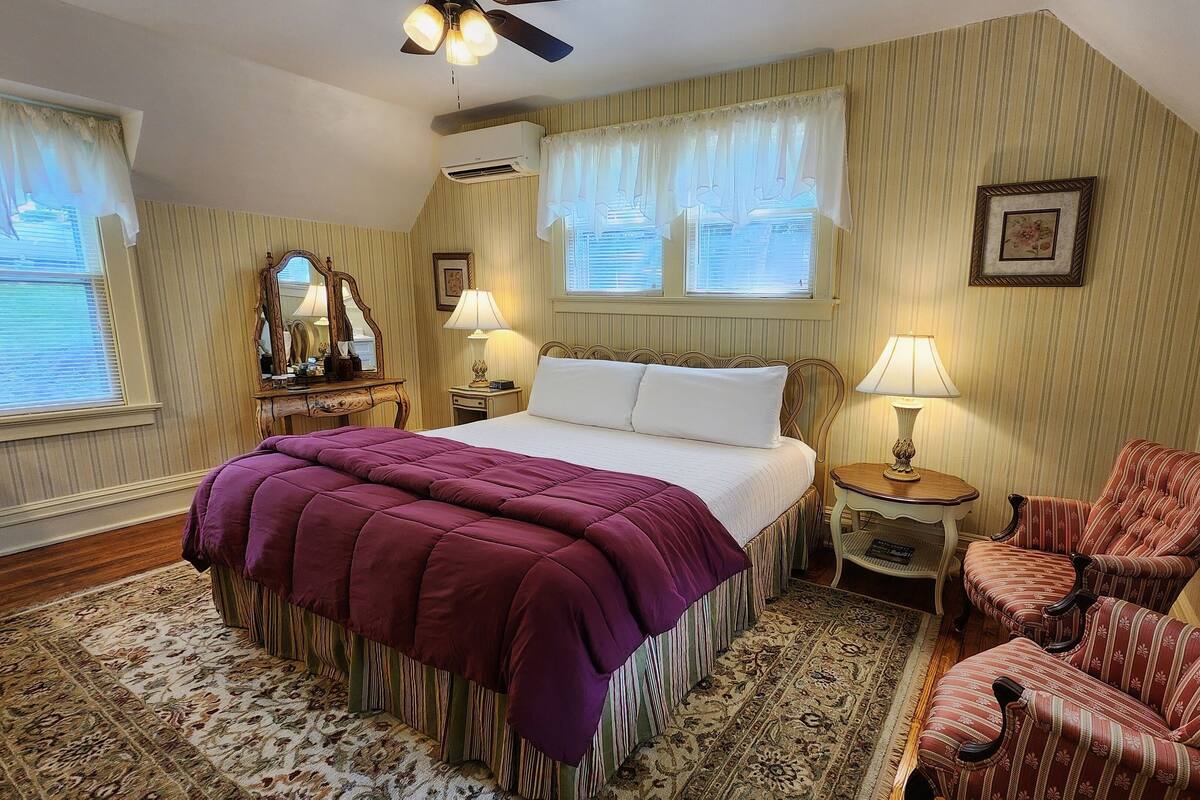 Un dormitorio con una cama grande, dos mesitas de noche, una silla y una ventana con cortinas.