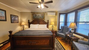 A well-lit bedroom with a large bed, a ceiling fan, and a window with blinds.