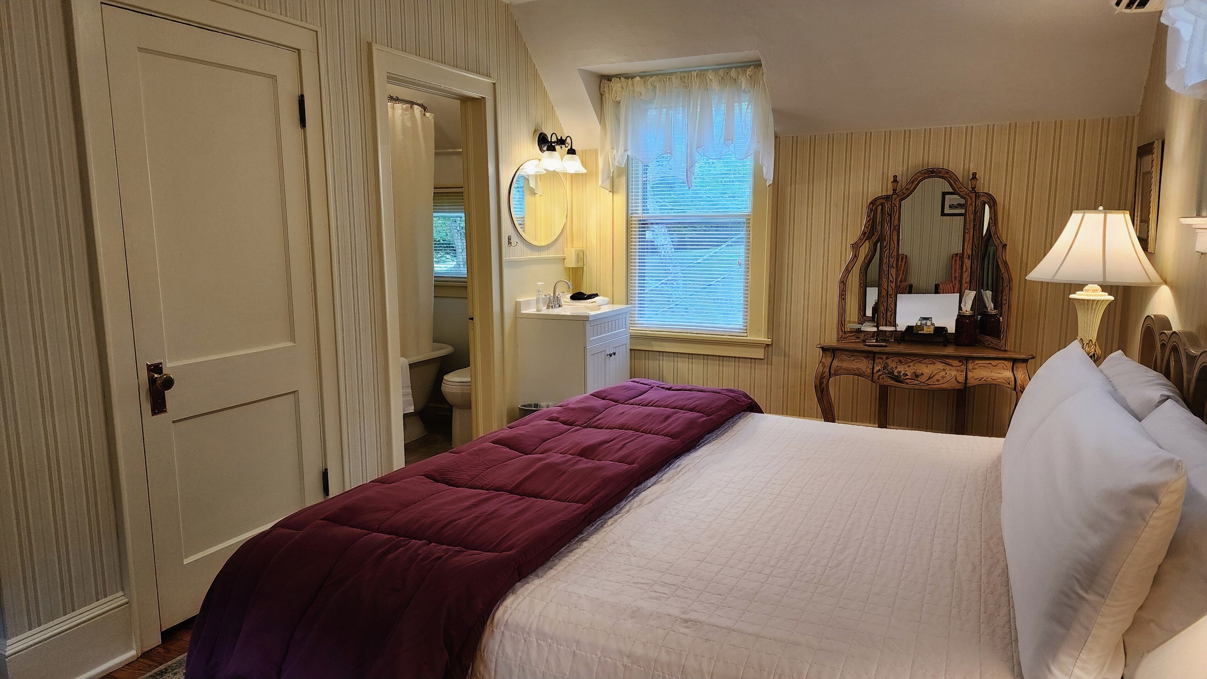 A bedroom with a bed, a dresser, a mirror, and a window with curtains.