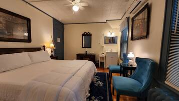 A hotel room with a large bed, a desk, a chair, a mirror, and a ceiling fan.