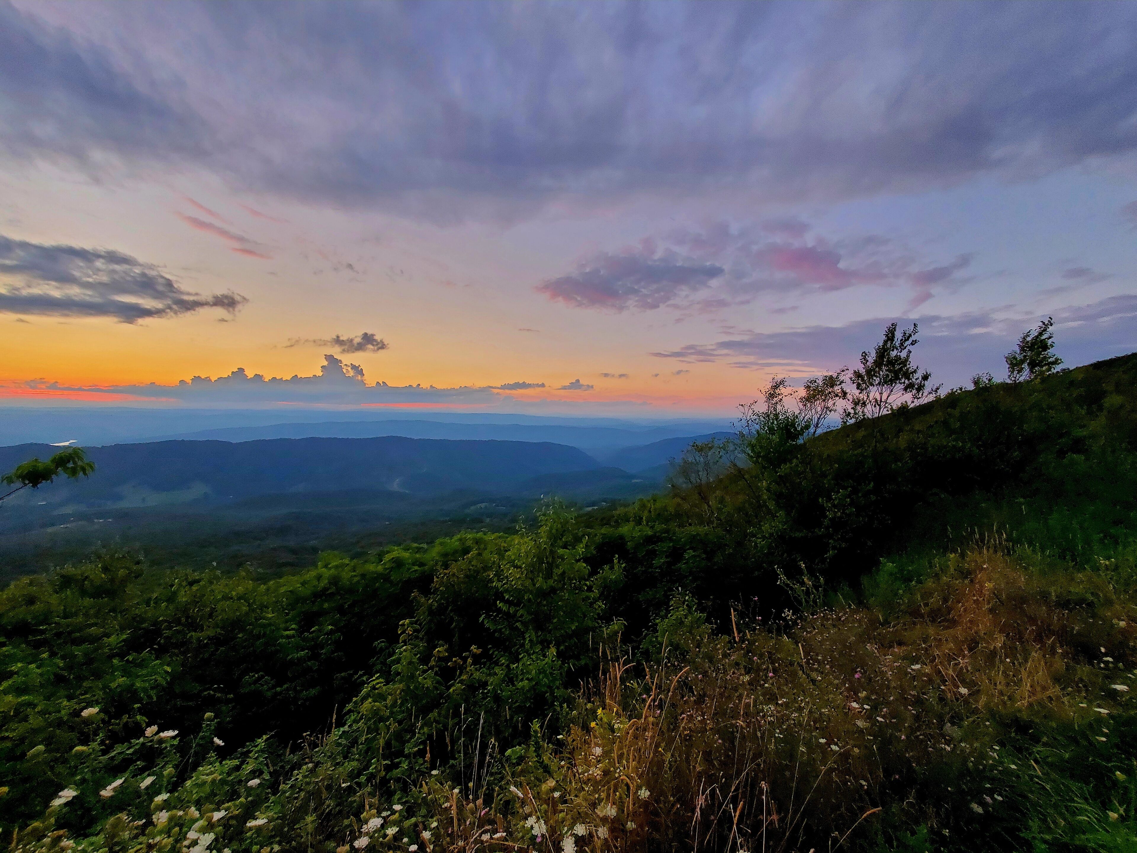 A panoramic view of a mountainous landscape with lush greenery and a clear sky at sunset.