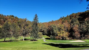 A golf course with a winding path, a pond, and autumn-colored trees. - Vine Cottage Inn (Hot Springs)