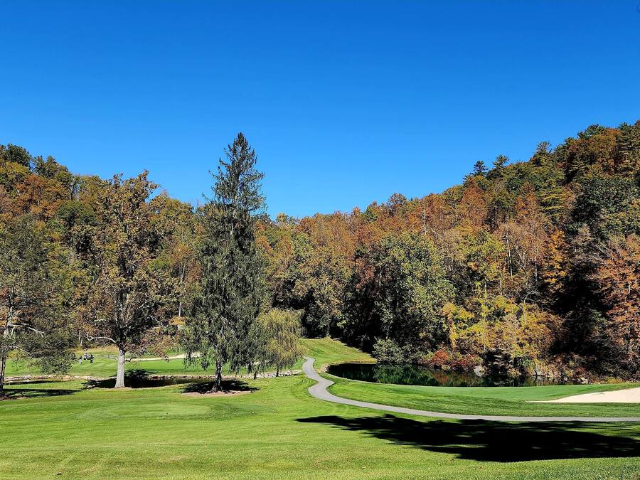 Un parcours de golf avec un sentier sinueux, un étang et des arbres aux couleurs automnales.