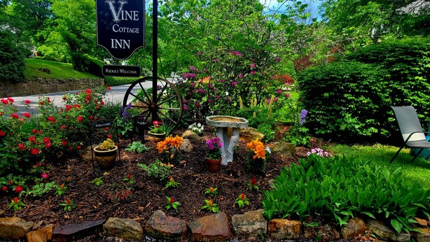 A garden area with a sign for Vine Cottage Inn, featuring a stone wall, flowering plants, and a decorative wheel. - Vine Cottage Inn (Hot Springs)