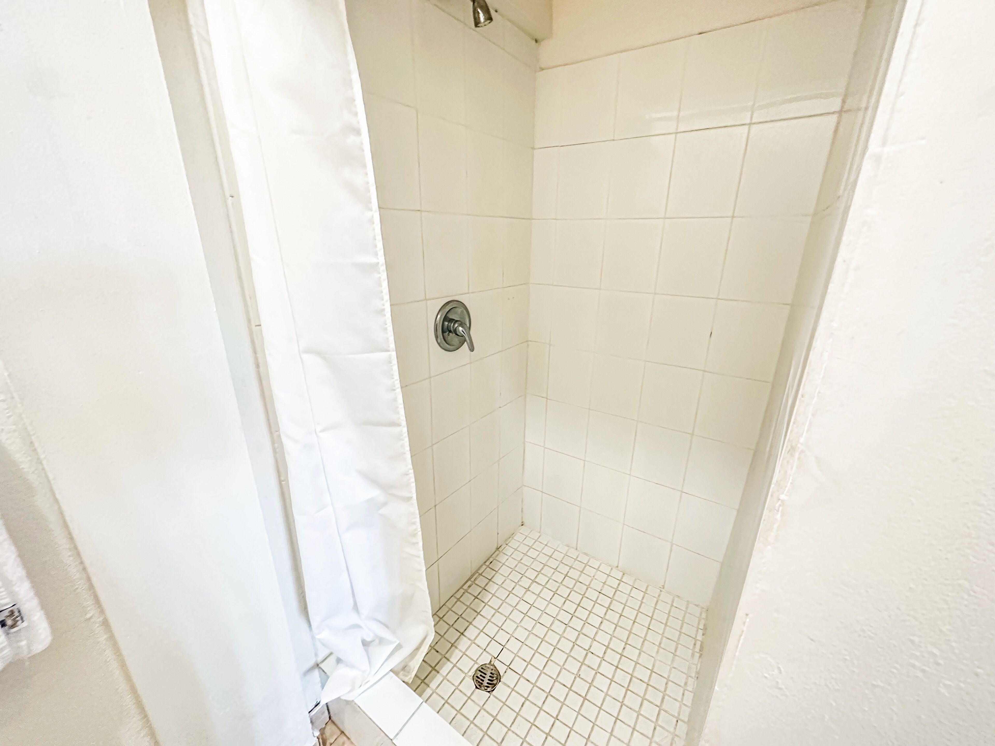 A small, white-tiled shower room with a showerhead and a drain.