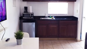 A compact kitchen with dark wooden cabinets, a white countertop, a built-in dishwasher, and a window providing natural light. - Boulevard 401 (Mayagüez)