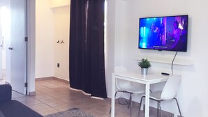 A modern living room with a ceiling fan, a flat-screen TV, a white table with two chairs, and a dark-colored sofa. - Boulevard 401 (Mayagüez)