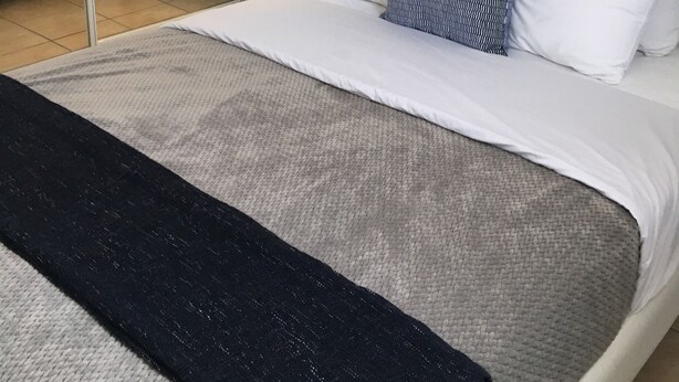 A neatly made bed with white and patterned pillows, a grey and black throw, and bedside lamps on white nightstands. - Boulevard 401 (Mayagüez)