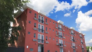 A red multi-story building with balconies, a parking lot, and a clear blue sky. - Boulevard 401 (Mayagüez)
