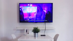 A modern living room with a flat-screen TV mounted on the wall, a white dining table with two chairs, and a small potted plant on the table. - Boulevard 401 (Mayagüez)