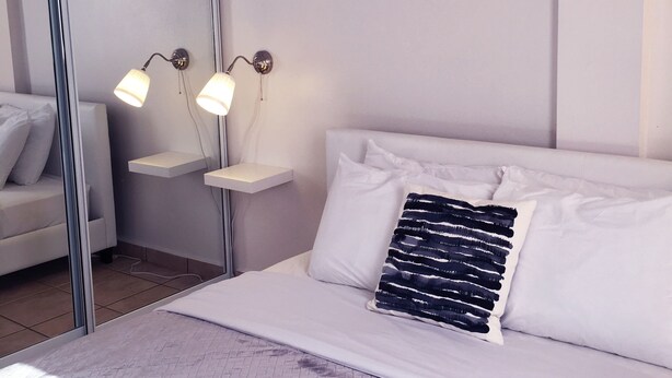 Une chambre moderne avec un grand lit, une table de chevet avec deux lampes, un miroir et une vue sur l’extérieur.
