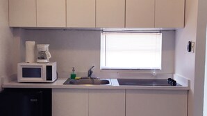 Une cuisine compacte avec des meubles blancs, un four à micro-ondes, un évier et un petit réfrigérateur.