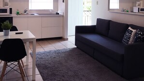 Une cuisine moderne avec des meubles blancs, une table à manger avec des chaises, un canapé foncé et un ventilateur de plafond.