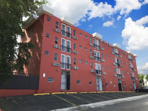 A red multi-story building with balconies, a parking lot, and a clear blue sky.