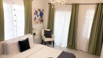Quarto de hotel com cama, uma cadeira, escrivaninha e lustre.