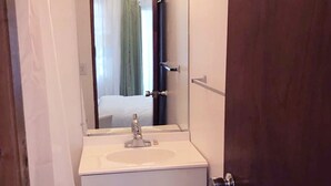A narrow bathroom with a white sink, a mirror, and a door. - Aibonito Hotel 201 (Aibonito)