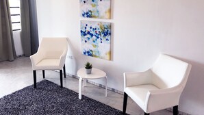 A modern room with two white armchairs, a small round table with a plant, and abstract art on the wall. - Aibonito Hotel 201 (Aibonito)