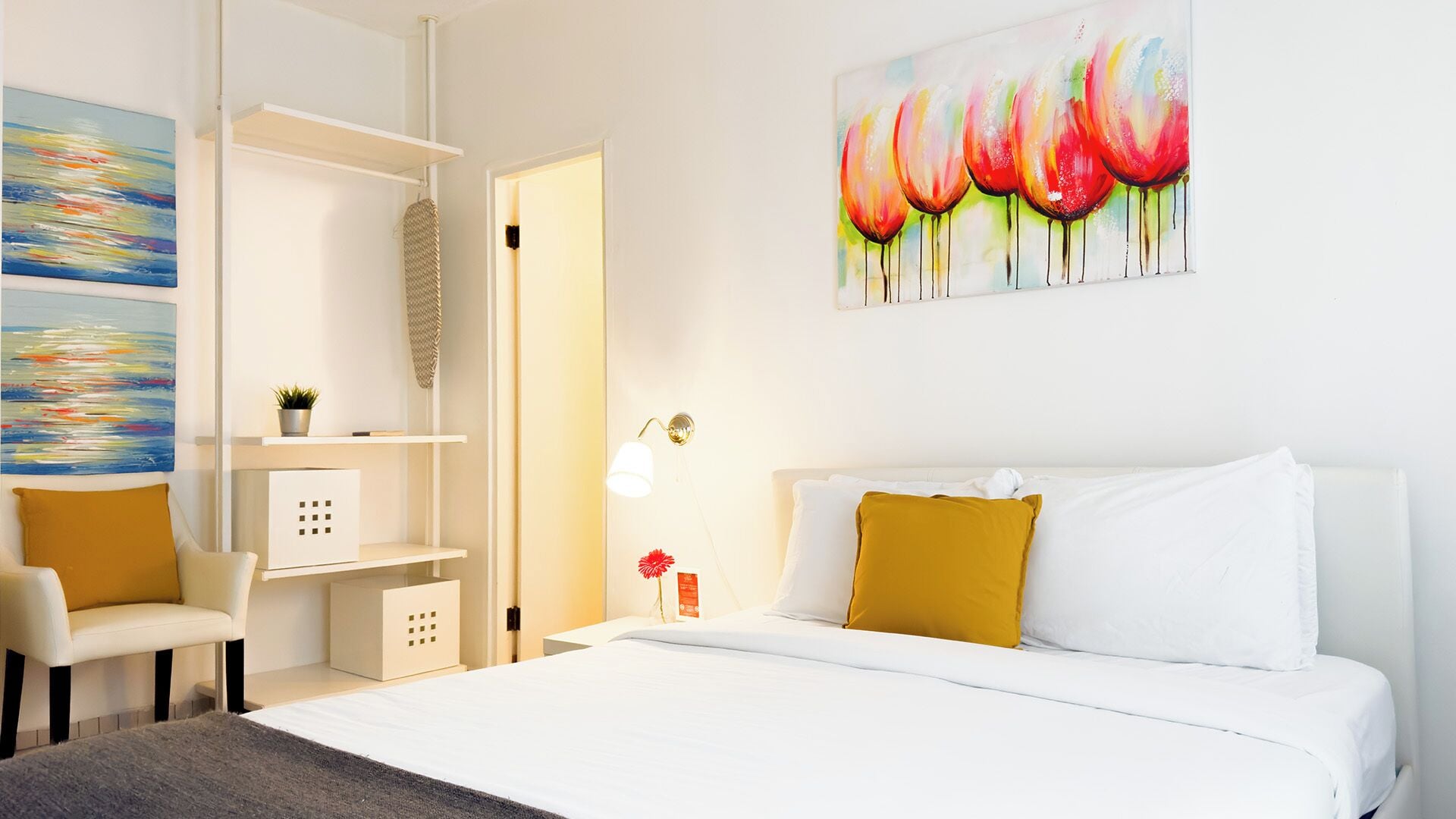 A hotel room with a bed, a chair, a desk, and shelves.