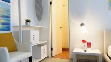 A modern hotel room with a white sofa, a small table with a lamp, a potted plant, and a painting on the wall.
