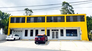 A two-story building with a yellow facade, a white garage door, and a red car parked in front. - Aibonito Hotel 203 (Aibonito)