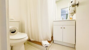 A small, clean bathroom with a toilet, a shower curtain, a sink with a mirror, and a cabinet. - Aibonito Hotel 203 (Aibonito)