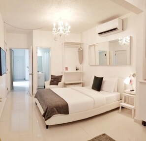 A modern bedroom with a large bed, a chandelier, an air conditioning unit, and a mirror. - Aibonito Hotel 204 (Aibonito)