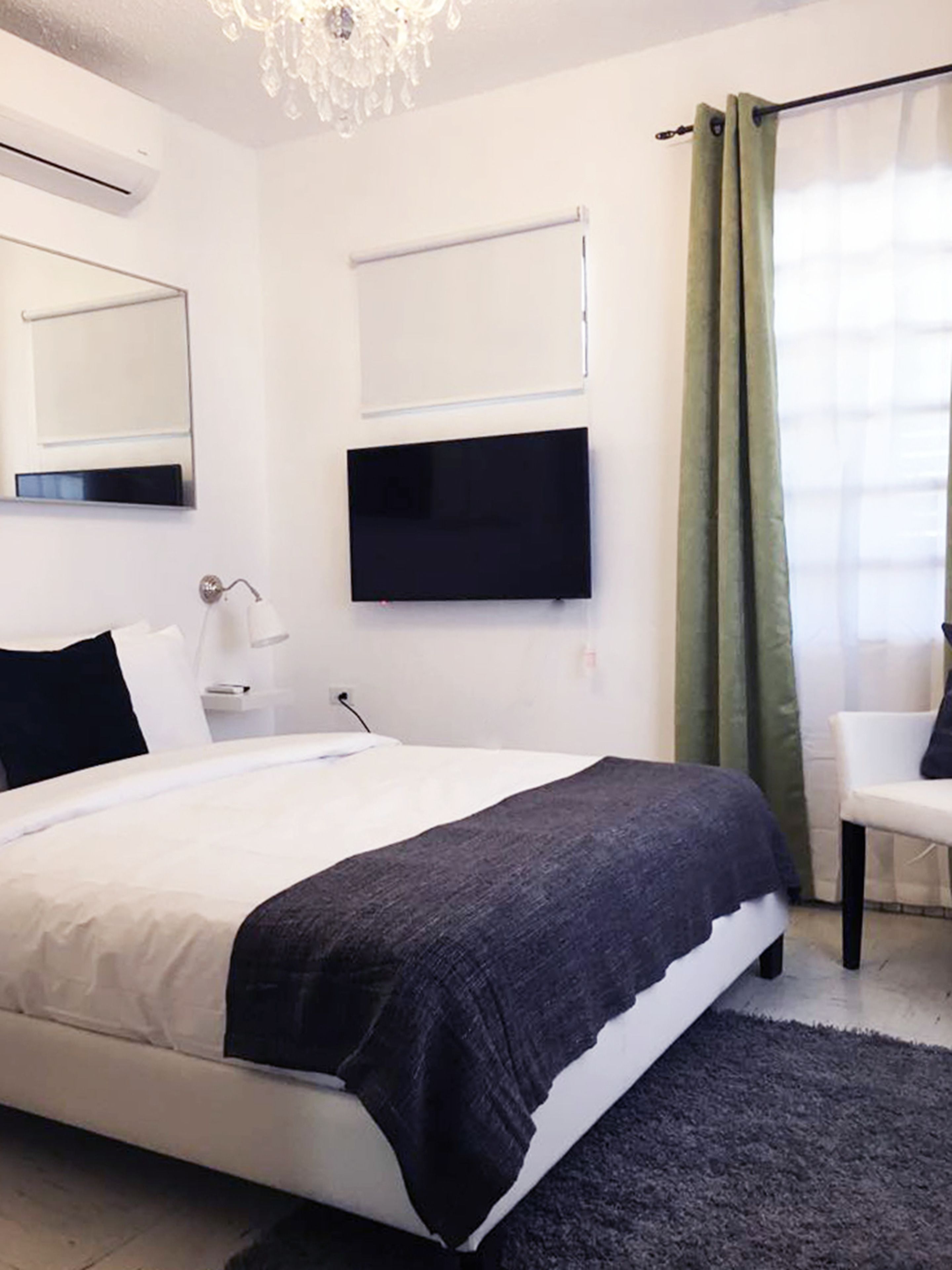 Een moderne slaapkamer met een bed, een flatscreen televisie, een nachtkastje, een lamp en een stoel.