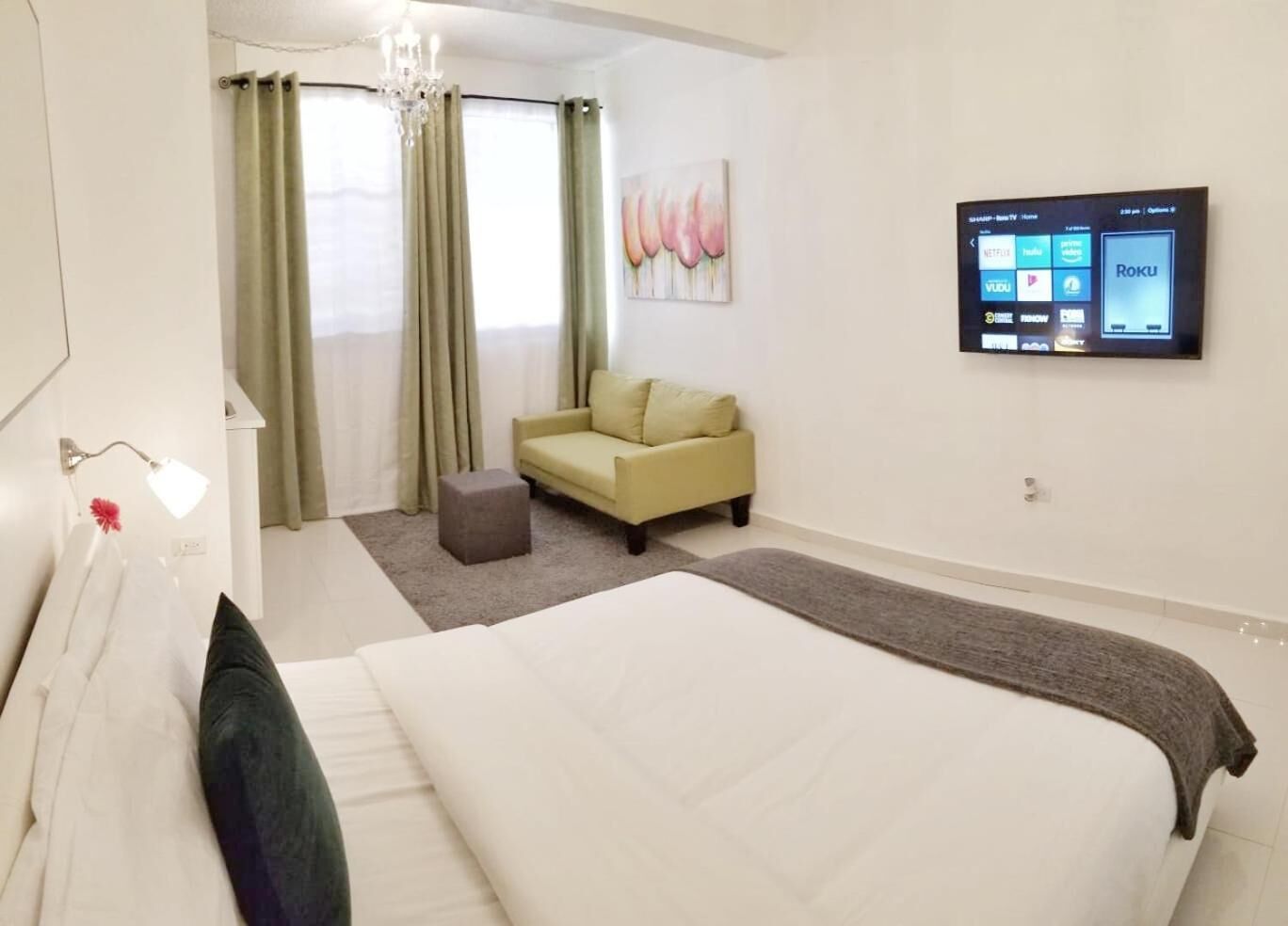 A hotel room with a large bed, a sofa, a TV mounted on the wall, and a window with curtains.