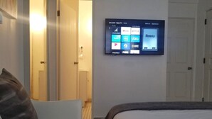 Et hotelværelse med en seng, en stol og et fjernsyn ophængt på væggen, der viser forskellige streamingtjenester.