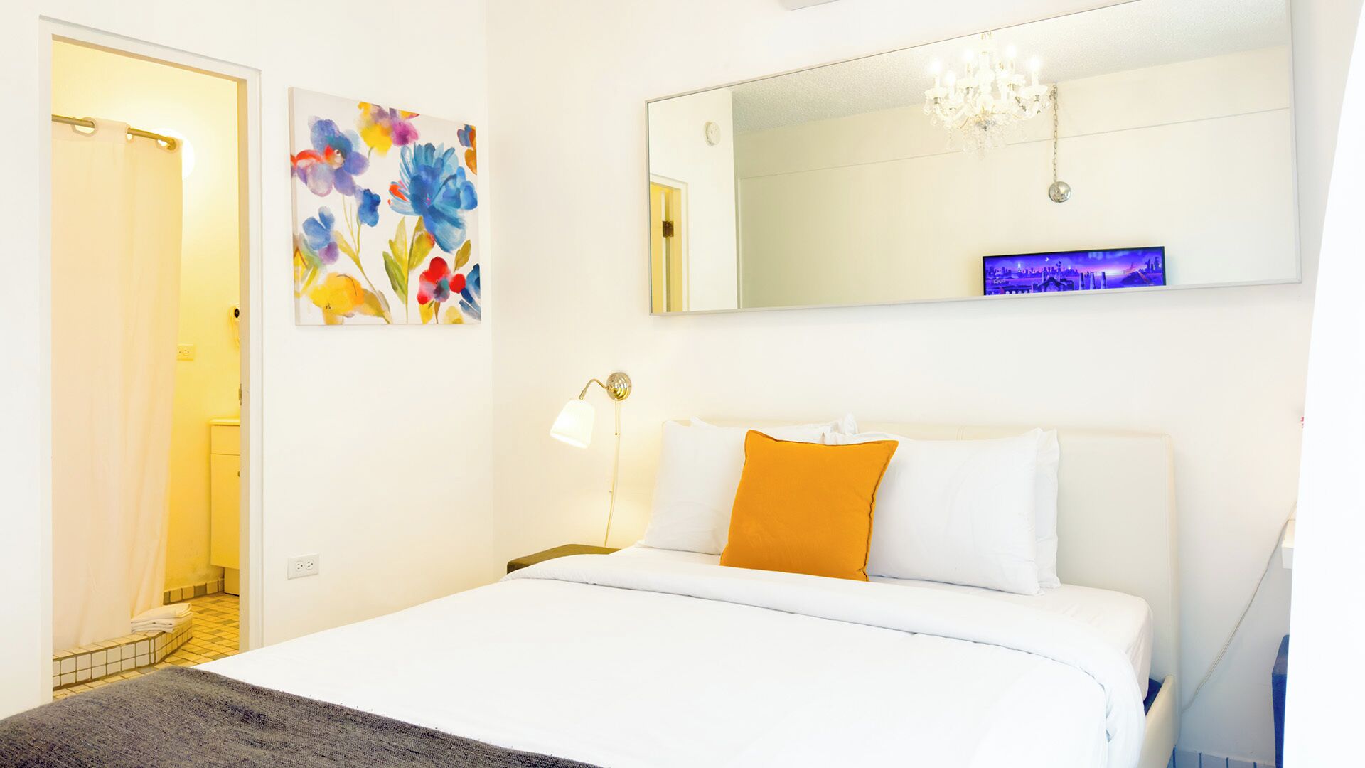 A hotel room with a bed, a nightstand, a lamp, a mirror, and a painting on the wall.