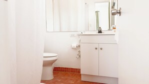 Uma casa de banho pequena e branca, com sanita, lavatório e espelho.