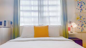 A hotel room with a bed, a bedside table with a lamp, a microwave, and a wall with a colorful abstract painting.