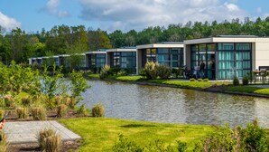 A row of modern buildings with large windows, a paved walkway, and a body of water in the foreground. - EuroParcs Buitenhuizen (Velsen-Zuid)