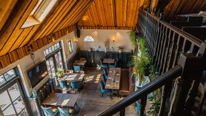 A high-ceilinged restaurant with wooden beams, large windows, and a staircase leading to an upper level. - EuroParcs Buitenhuizen (Velsen-Zuid)