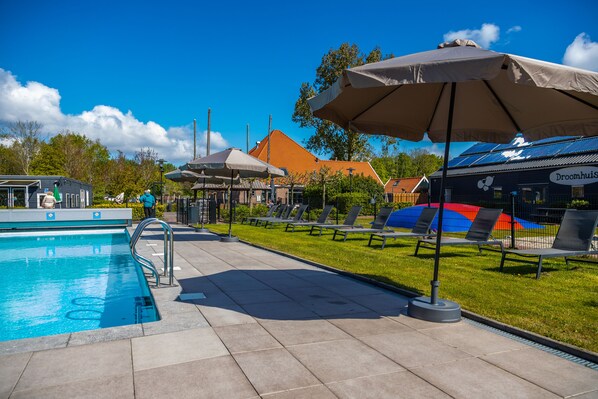 A swimming pool with lounge chairs and umbrellas, a building with a sign reading "Droomhuis," and a clear blue sky. - EuroParcs Buitenhuizen (Velsen-Zuid)