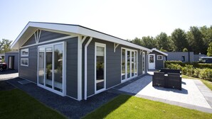 A modern house with a sloped roof, large glass windows, and a paved driveway. - EuroParcs Buitenhuizen (Velsen-Zuid)