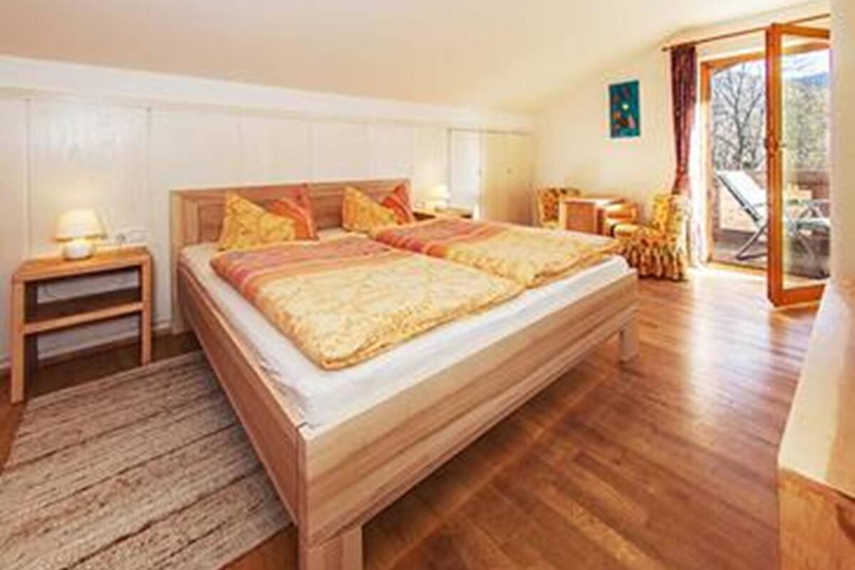 A bedroom with a wooden bed, a nightstand, a window with curtains, and a view of the outdoors.