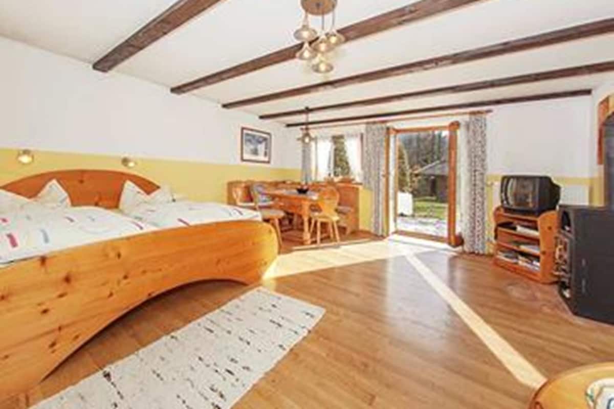 A bedroom with a wooden bed, a desk, a television, and a sliding glass door leading to a balcony.