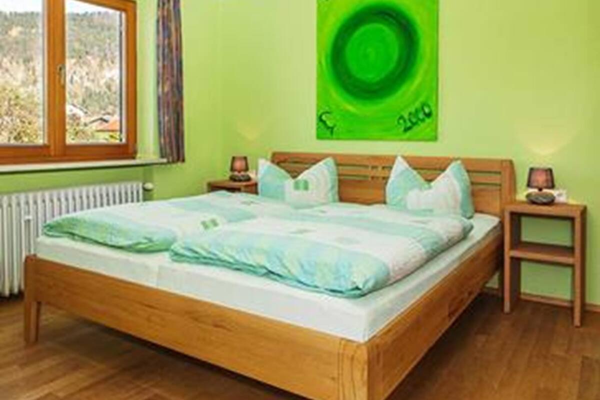 A bedroom with a wooden bed, a green wall, a window with curtains, and a green artwork.