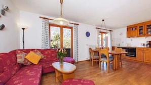 Un salon chaleureux avec un canapé rouge, une table basse en bois et un coin repas comprenant une table et des chaises en bois.