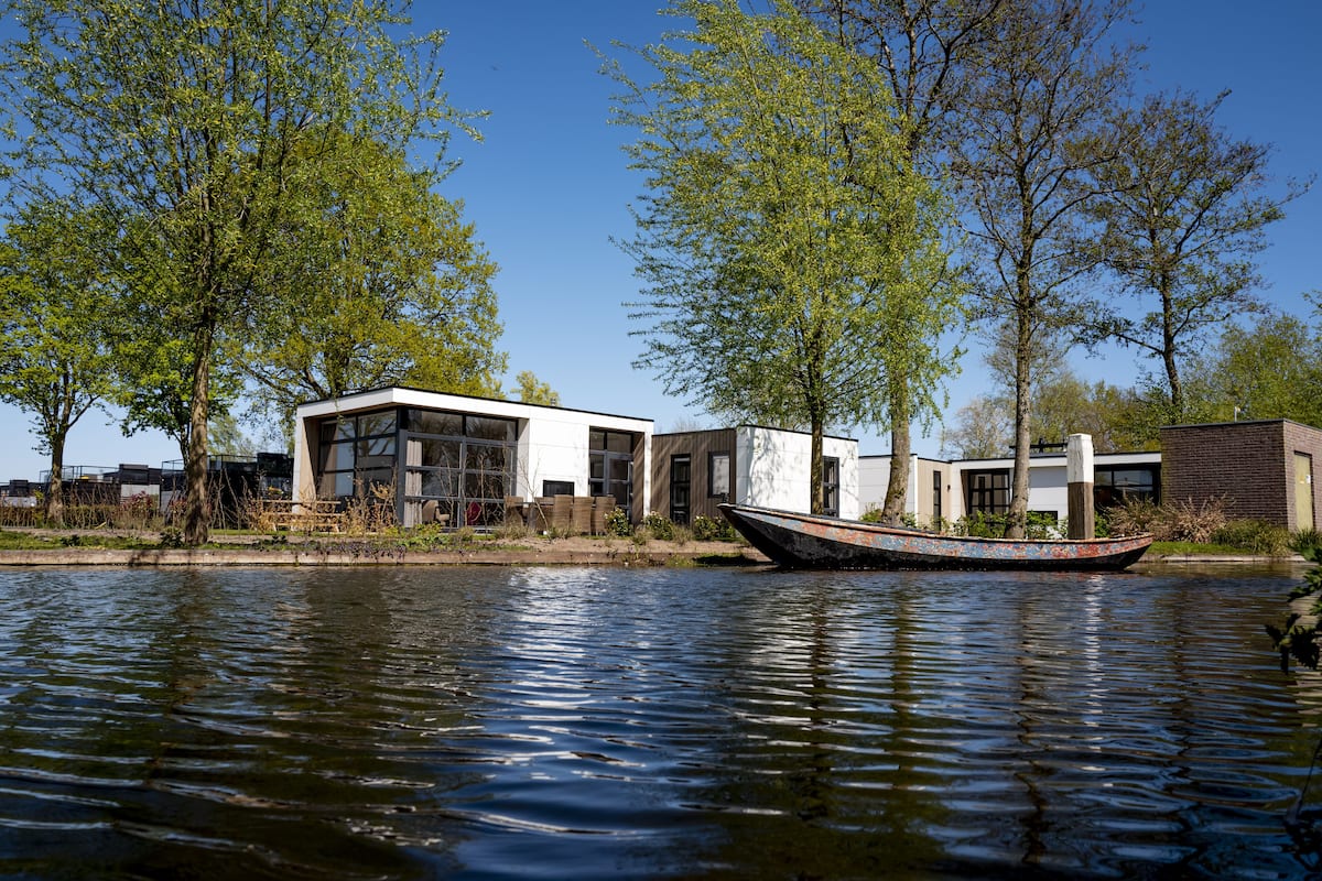 Una propiedad junto al río con arquitectura moderna, un barco amarrado cerca del agua y abundante vegetación.