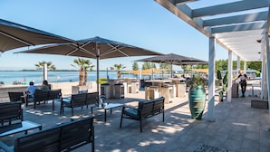 An outdoor patio with seating, umbrellas, and a view of the water. - EuroParcs Bad Hoophuizen (Hulshorst)