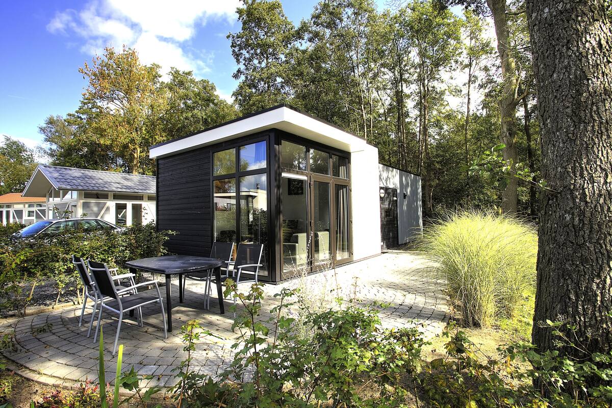 Una casa moderna con un patio amueblado con mesa y sillas, rodeado de árboles y plantas.
