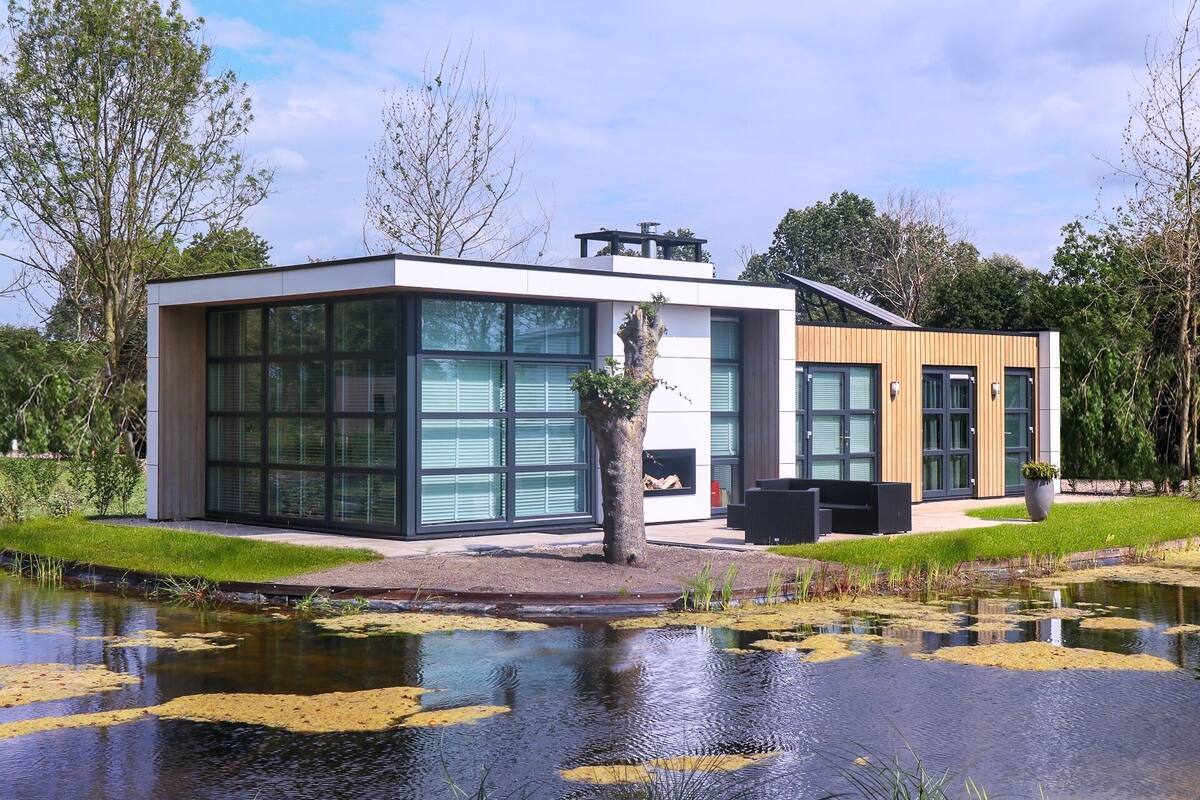 Un edificio moderno con amplios ventanales de vidrio, fachada de madera y un pequeño estanque al frente.