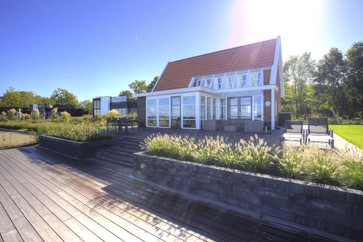 Una casa moderna con un amplio ventanal, una terraza de madera y un muro de ladrillo.