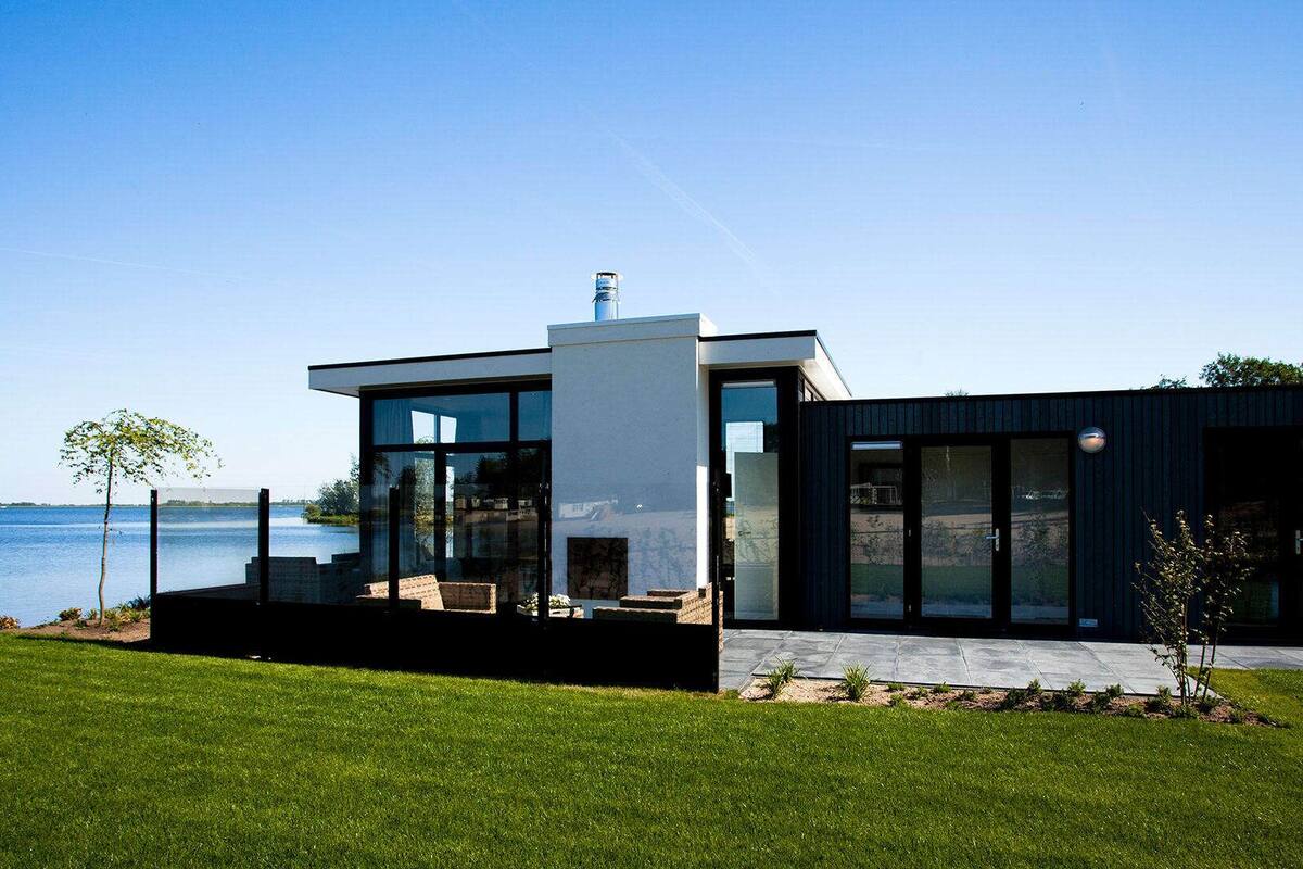 Una casa moderna con un amplio muro de cristal, una pequeña terraza y vista al agua.