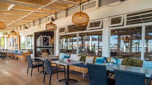 An indoor dining area with wooden flooring, wicker chairs, and tables. Large windows provide views of the outdoors. - EuroParcs Bad Hoophuizen (Hulshorst)