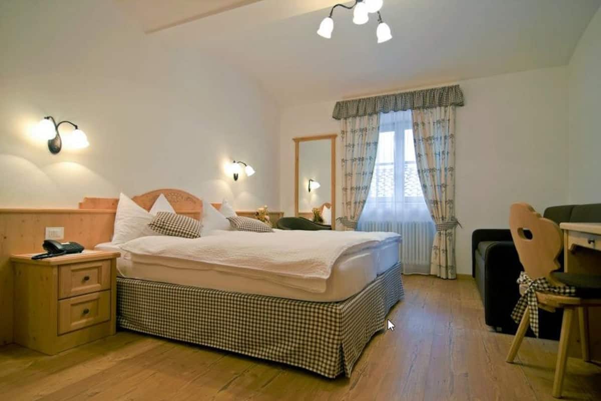 Ein Schlafzimmer mit Bett, Nachttischen, einem Sessel, einem Schreibtisch und einem Fenster mit Vorhängen.